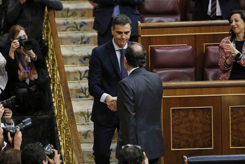 El presidente del gobierno español Mariano Rajoy, de espaldas, estrecha la mano del líder socialista Pedro Sánchez luego de una moción de desconfianza en el paramento en Madrid. (AP)