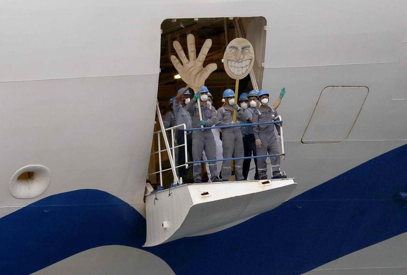 Tripulantes del crucero Ruby Princess saludan agitando una mano y una cara de cartón, mientras el barco se aleja del puerto de Kembla en Wollongong. (AP)