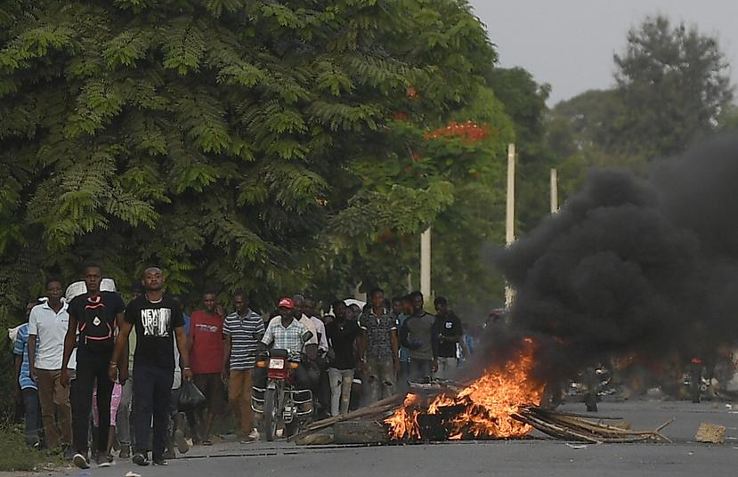 Varios hombres caminan junto a una barricada en llamas después de que cientos de trabajadores huyeran de una zona en la que se llevaron a cabo manifestaciones que se tornaron violentas cerca de la ciudad natal del difunto presidente Jovenel Moïse.
