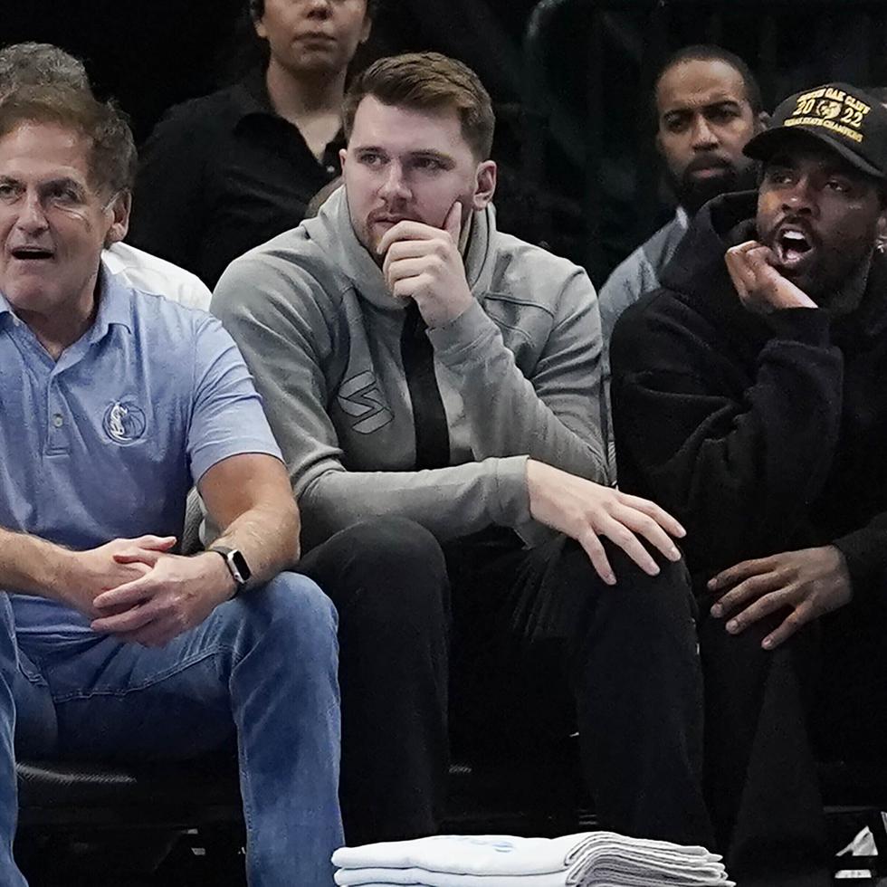 Mark Cuban, a la izquierda, dueño de los Mavericks de Dallas, aparece sentado junto a los jugadores Luka Doncic (centro) y Kyrie Irving.