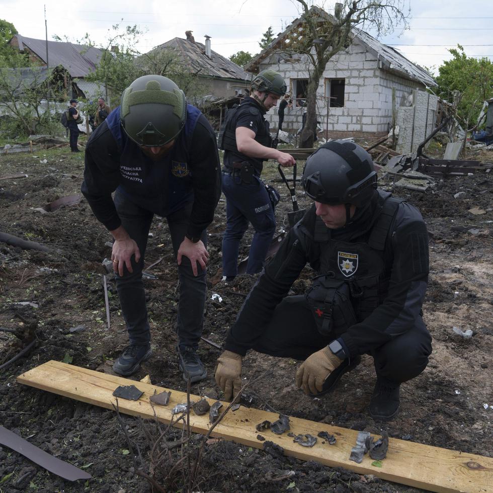 Un policía ucraniano y un fiscal de crímenes de guerra analizan fragmentos de una bomba frente a una residencia dañada después de un ataque aéreo ruso contra un vecindario residencial, el sábado 18 de mayo de 2024, en Járkiv, Ucrania.