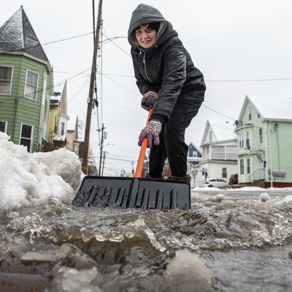 Amber Vallee pushes water down Walnut Street in Lewiston, Maine, Saturday morning, Jan 13, 2024, after snow turned to rain during yet another storm of mixed precipitation hit the area. "I wish it was all snow. I'm tired of this slush that will turn into ice at the bottom of our driveway." she said while keeping a path open for the rain and melting snow to flow into a nearby storm drain. (Russ Dillingham/Sun Journal via AP)