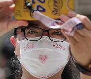 Una mujer con mascarilla para protegerse del nuevo coronavirus graba a los estudiantes que salen de la escuela tras completar el primer día de los exámenes de acceso a la universidad, conocidos como gaokao, en Beijing, China, el martes 7 de julio de 2020. Los exámenes se aplazaron un mes por la pandemia del coronavirus.  (AP Foto/Andy Wong)