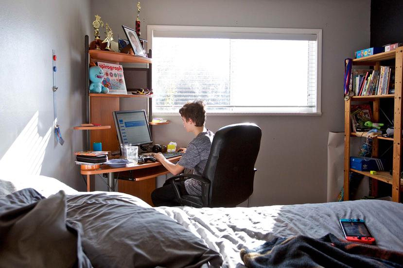 Un niño toma sus clases en línea desde su cuarto. (AP)
