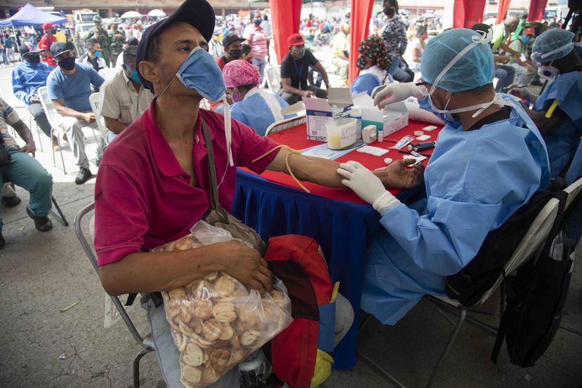 Un trabajador de salud le toma una muestra de sangre para una prueba rápida de COVID-19 a un hombre que trabaja vendiendo galletas en el mercado de alimentos de Coche en Caracas, Venezuela, el martes 23 de junio de 2020. (AP/Ariana Cubillos)