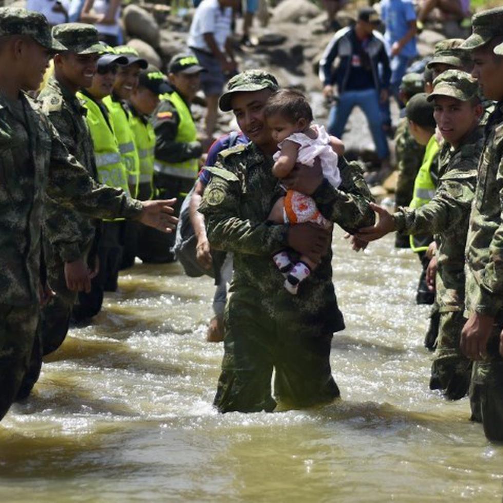 Un bebé es cargado por un militar al cruzar la frontera en el río Táchira. Cientos de colombianos están siendo deportados de Venezuela. (AFP)