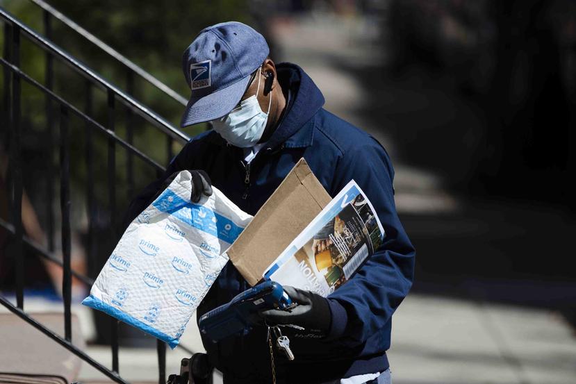 Un empleado del Servicio Postal de Estados Unidos hace una entrega con guantes y mascarilla en Filadelfia, el jueves 2 de abril de 2020. (AP / Matt Rourke)