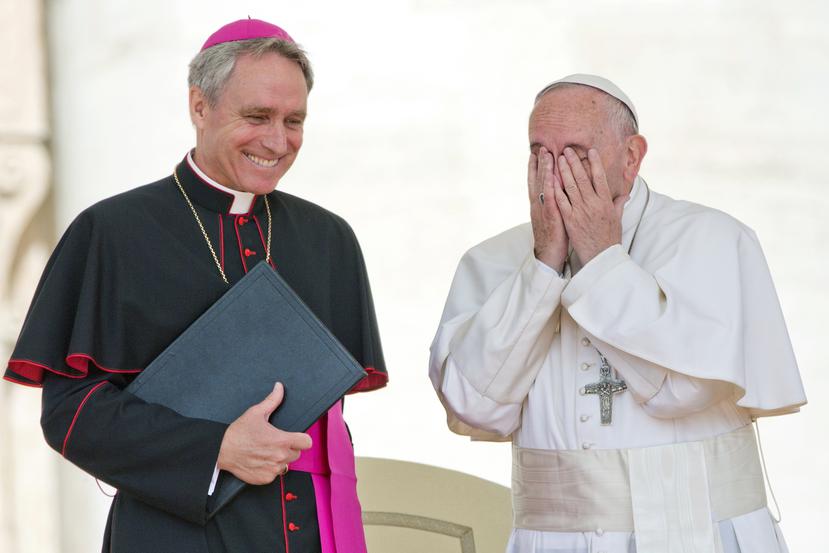 El papa Francisco se lleva las manos a la cara mientras el secretario personal del fallecido papa emérito Benedicto XVI sonríe.