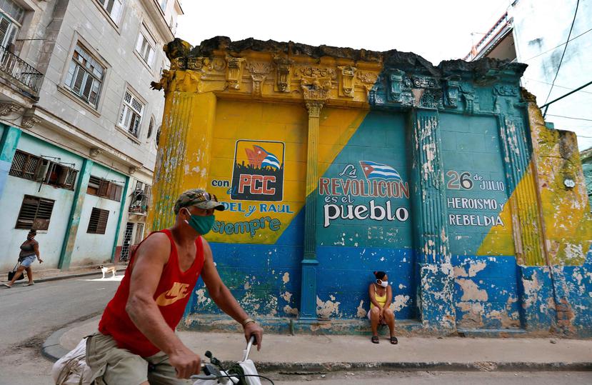 Un hombre con tapabocas en bicicleta pasa junto a una pared con un grafiti político este miércoles, en La Habana. (Agencia EFE)