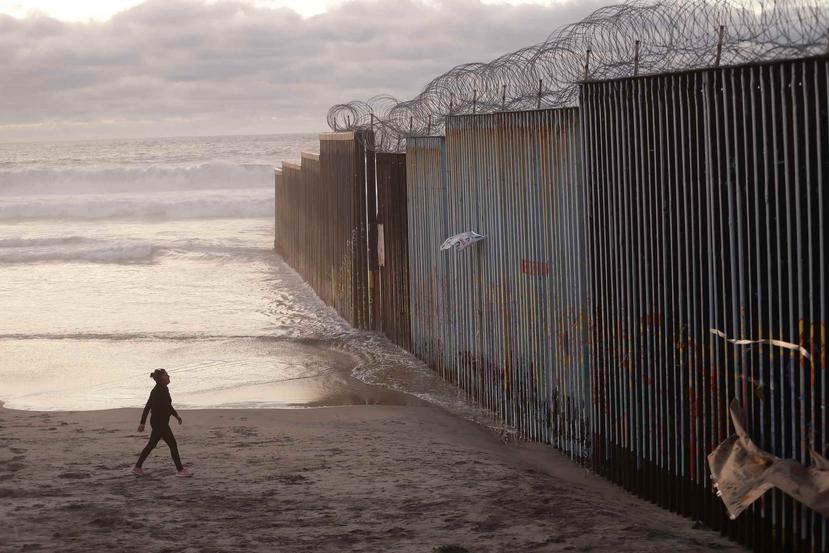 Fotografía de archivo del 9 de enero de 2019 de una mujer caminando en la playa junto al muro fronterizo con alambres de púas en Tijuana, México. (AP Foto/Gregory Bull)