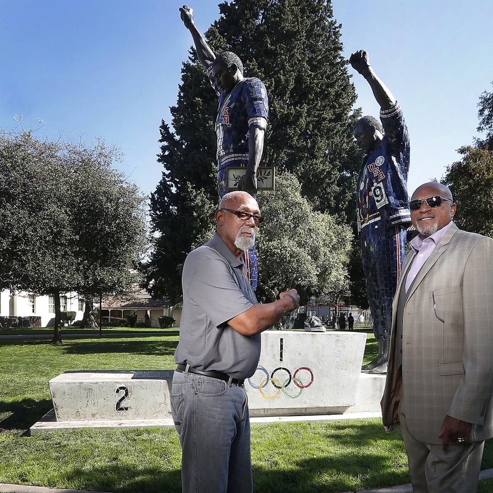 En esta foto del 17 de octubre de 2018, John Carlos (izquierda) y Tommie Smith posan frente a la estatua que los muestra con el puño en alto, la señal de protesta que hicieron en el podio de los Juegos Olímpicos de México 1968. La estatua se encuentra en el campus de la Universidad Estatal de San José, en California.