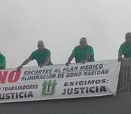 Cuatro empleados de la Autoridad de Acueductos y Alcantarillados (AAA) sostienen una pancarta en la que rechazan los recortes propuestos por la Junta de Supervisión Fiscal. (Suministrada)