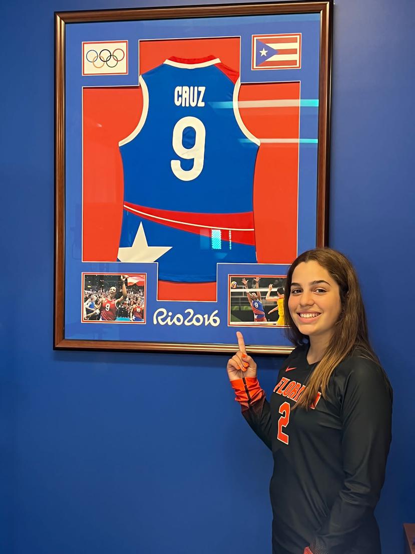 Gabriela Cornier posa junto a una camiseta de Aury Cruz del Equipo Nacional, la cual está enmarcada en una de las padres de la instalación deportiva de la Universidad de Florida.