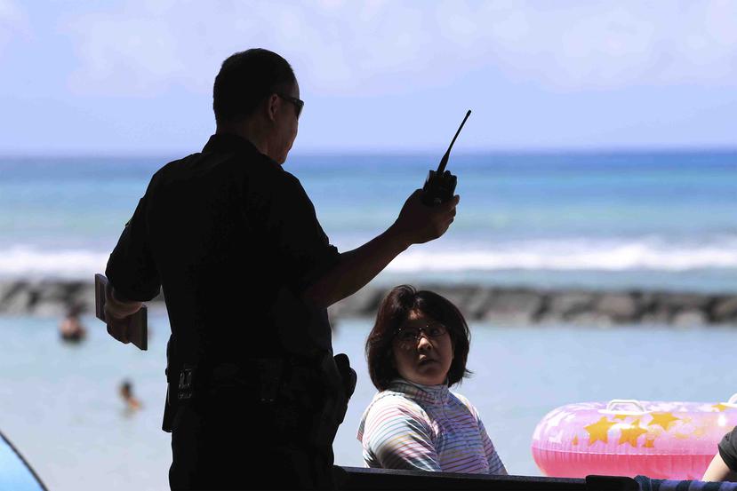 Un oficial de la Policía en Hawai informa a turistas que las playas han sido cerradas para evitar el contagio del coronavirus COVID-19. (AP)