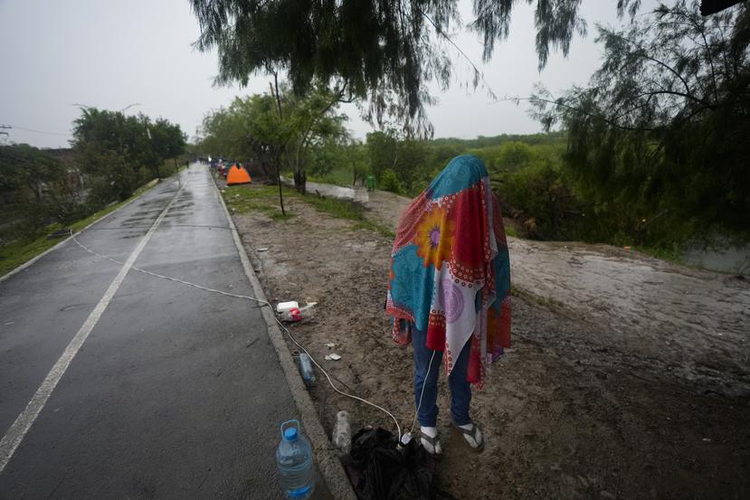 Un migrante venezolano de pie cubierto con una manta mientras escribe un mensaje de texto, en la orilla del río Bravo (Grande) en Matamoros, México, el sábado 13 de mayo de 2023.