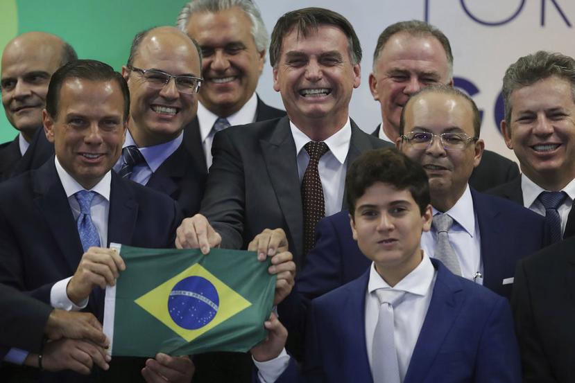 El presidente electo de Brasil Jair Bolsonaro (centro) posa ante los fotógrafos junto con los gobernadores electos, mientras sostiene una bandera brasileña. (AP/Eraldo Peres)