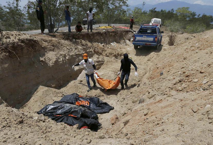 Rescatistas cargan los cadáveres para enterrarlos en una fosa común. (AP)