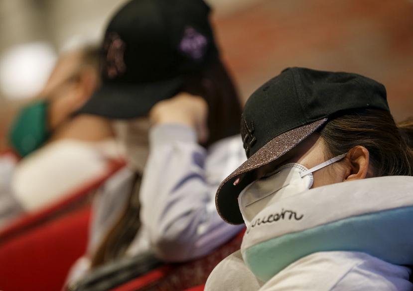 Una mujer duerme con mascarilla y tapando su rostro en el aeropuerto Changi de Singapur.