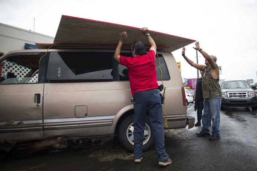 Varios hombres colocan un panel de madera sobre una guagua como preparativo al paso del huracán Irma. (GFR Media)