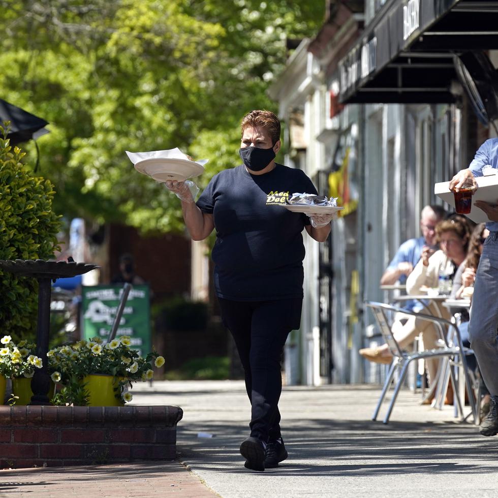 Une empleada de restaurante Mediterranean Deli lleva platillos a los comensales en el área de terraza, en Chapel Hill, Carolina del Norte, el viernes 16 de abril de 2021. (AP Foto/Gerry Broome)