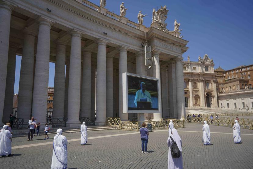 Monjas y fieles respetan el distanciamiento social mientras observan al papa Francisco recitar una oración a través de una pantalla en la plaza de San Pedro, en el Vaticano. (AP)