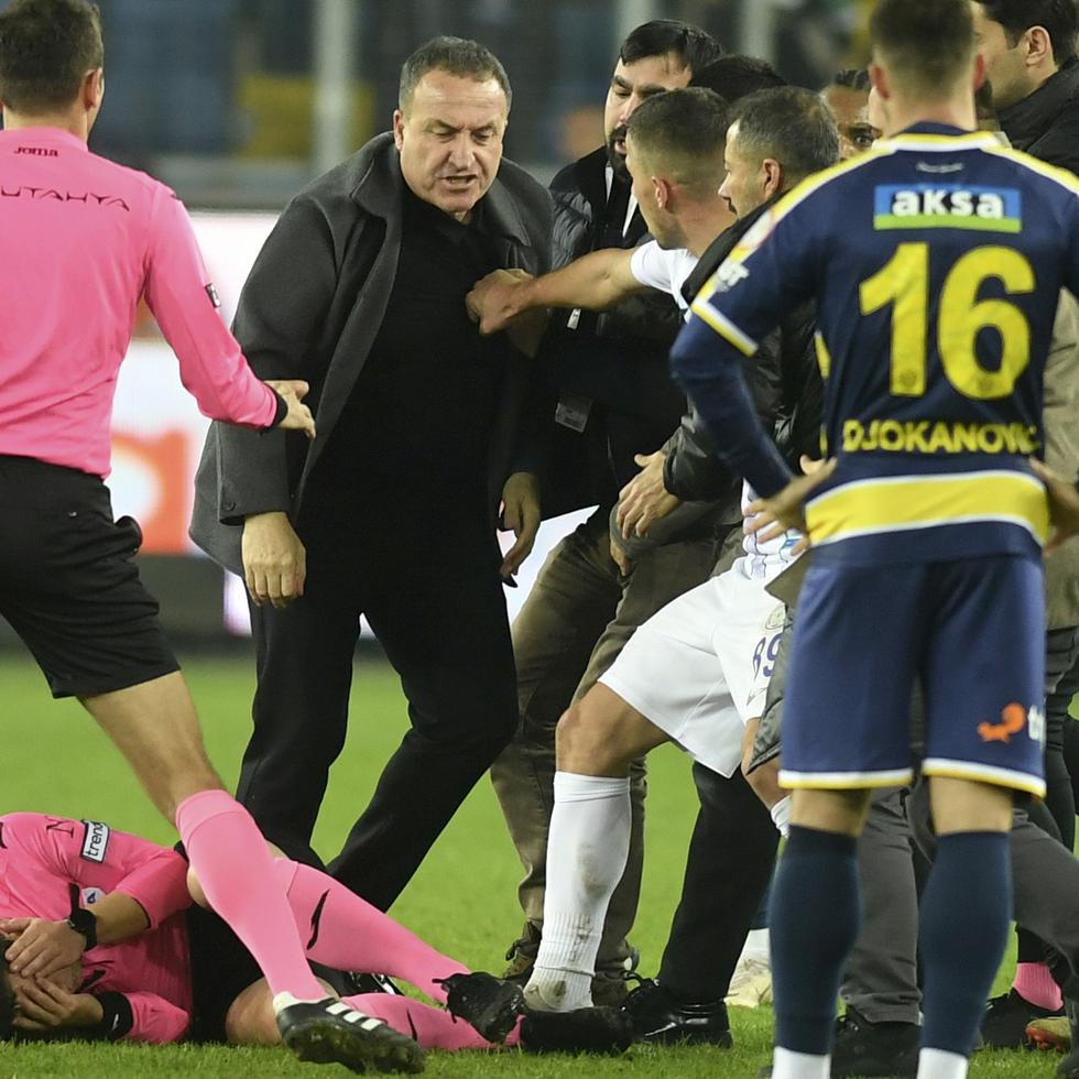 El árbitro Halil Umut se tapa el rostro en el césped tras recibir un golpe de Faruk Koca, al centro y de pie.