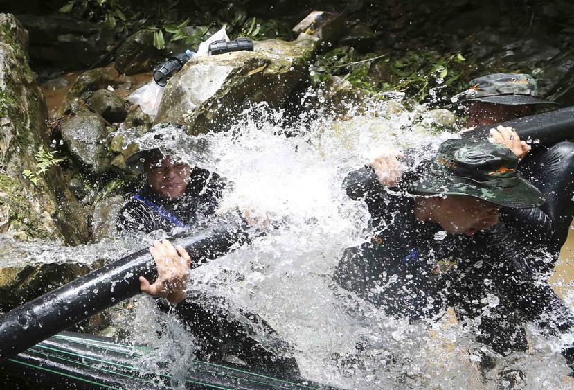 Dos soldados intentan conectar unos tubos para ayudar a desviar el flujo de agua en la cueva donde quedaron atrapados los niños en Tailandia. (AP)
