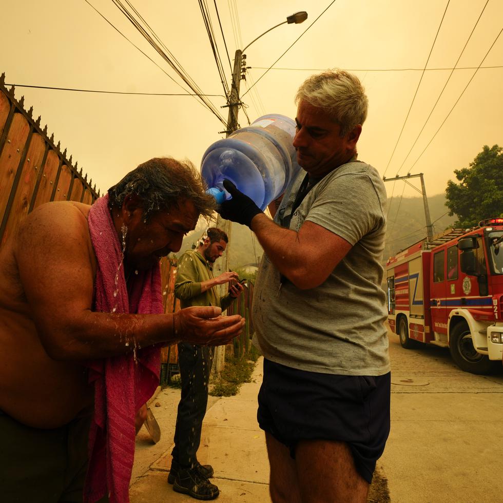 Una persona ayuda a su vecino a enfriarse mientras un fuego forestal se desarrolla en una zona cercana a Viña del Mar.