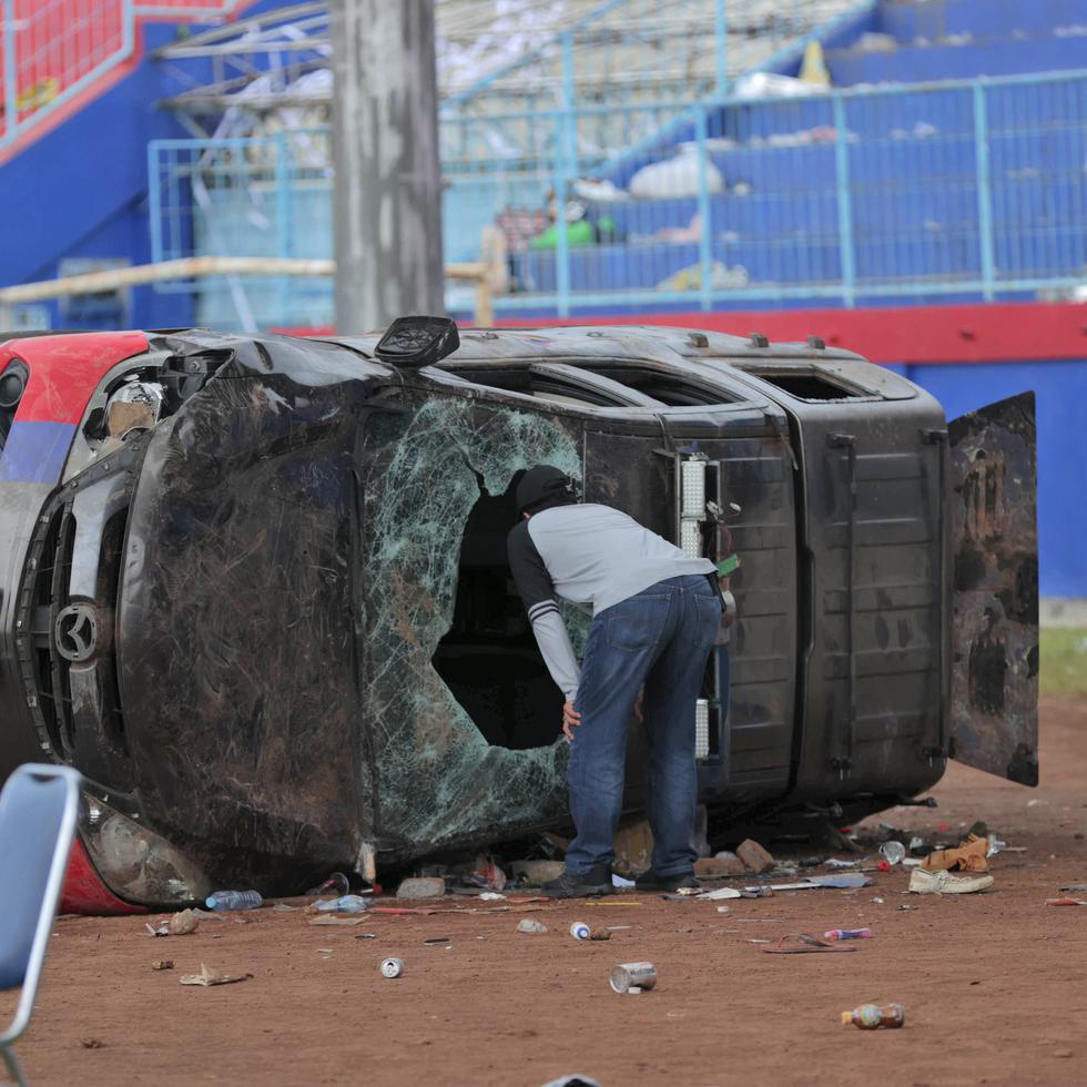 Un oficial de policía vestido de civil inspecciona un automóvil policial destrozado en disturbios de fútbol en el estadio Kanjuruhan en Malang, Java Oriental, Indonesia.