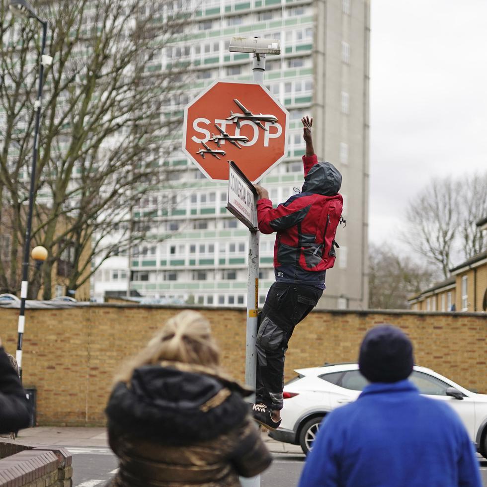 Una persona retira una obra de arte de Banksy que parece mostrar tres drones sobre un cartel de pare que fue develado en la intersección de las calles Southampton Way y Commercial Way en Peckham, sureste de Londres, el viernes.