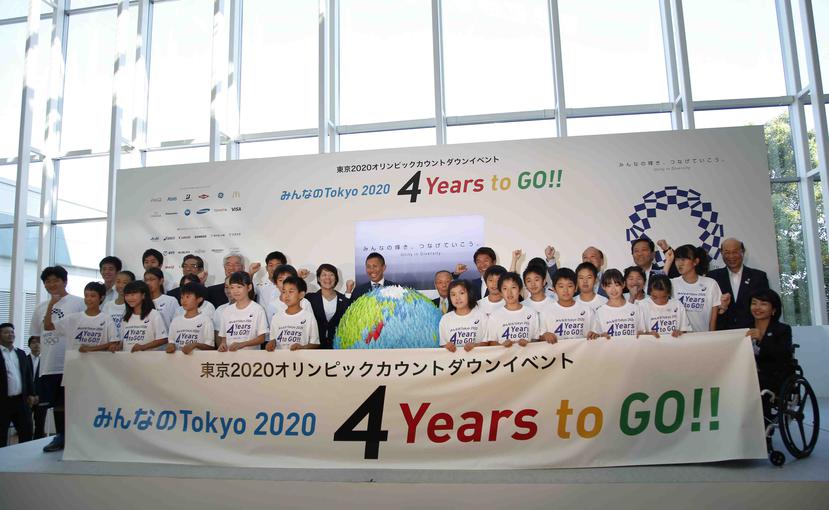 Organizadores de los Juegos de Tokio 2020 posan con niños en el aeropuerto de Haneda, junto a una pancarta con el conteo regresivo para la justa. (AP / Shizuo Kambayashi)