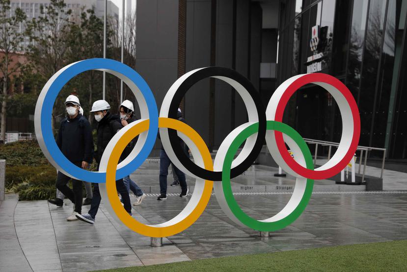 Un grupo de personas con mascarillas pasa detrás de los anillos olímpicos en Tokio. (AP)