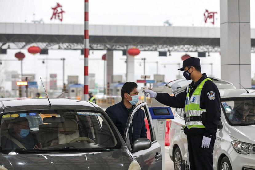 Un policía usa un termómetro digital para chequear la temperatura de un automovilista en un punto de peajes en una carretera en Wuhan, en el centro de China. (Chinatopix vía AP)