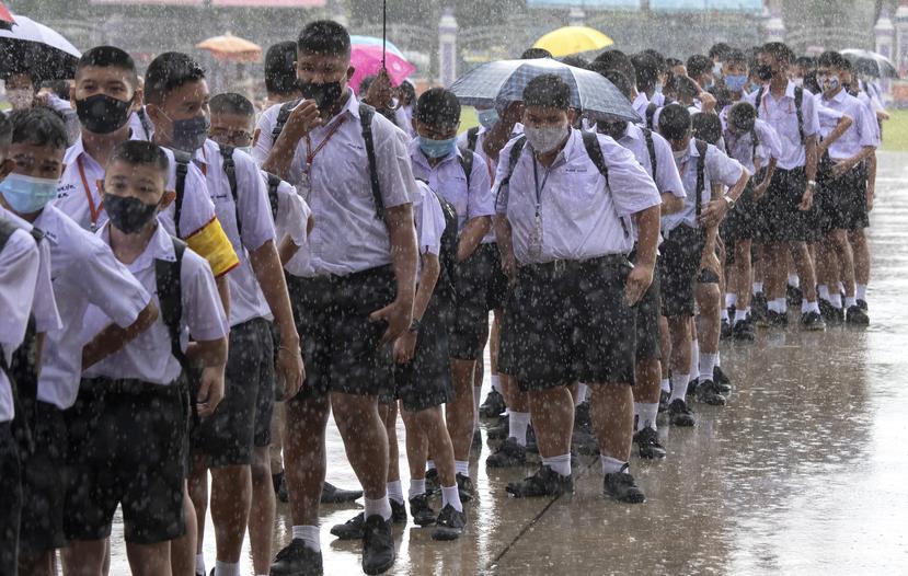 Estudiantes utilizan una mascarilla contra posibles contagios mientras esperan bajo la lluvia para entrar a su escuela en Tailandia.