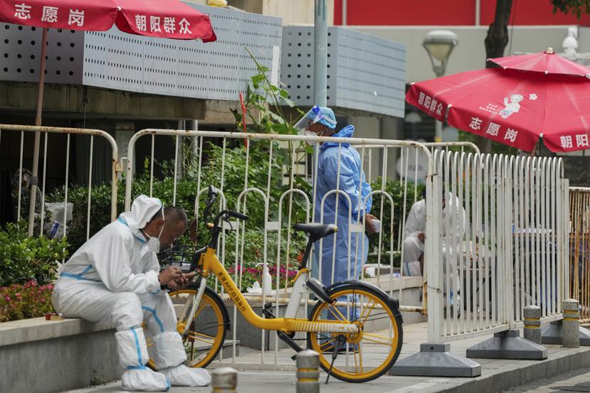 Trabajadores observan un vecindario que fue aislado como parte de las restricciones implementadas por un nuevo brote de COVID-19 en Pekín, el lunes 13 de junio de 2022.