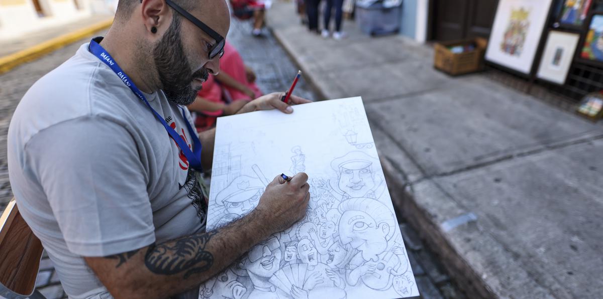 El artista Eduardo “Poty” Rosado realiza uno de sus dibujos desde una silla en la calle San Sebastián. Rosado lleva cerca de 20 años en las artes gráficas.