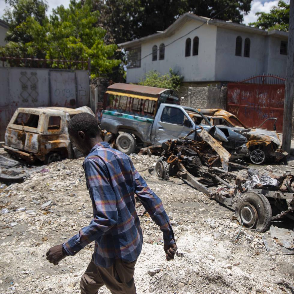 A man walks past charred and abandoned vehicles in La Plaine neighborhood of Port-au-Prince, Haiti, Friday, May 6, 2022. Fighting raged in four districts on the northern side of Port-au-Prince that has surged as increasingly powerful gangs try to control more territory during the political power vacuum left by the July 7 assassination of President Jovenel Moise. (AP Photo/Odelyn Joseph)