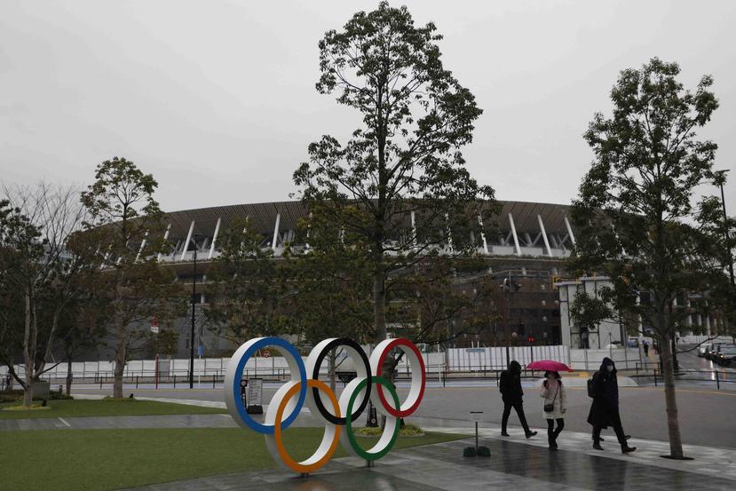 Unas personas caminan frente a los aros olímpicos cerca del estadio nacional de Tokio. (AP)