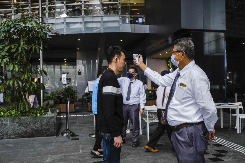En esta imagen, tomada el 16 de marzo de 2020, un hombre toma la temperatura a una visitante antes de entrar a la Plaza Asia Tower en Singapur. (AP)