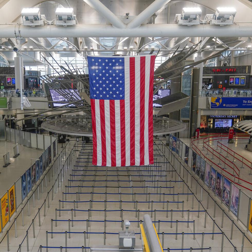 Una bandera estadounidense cuelga sobre la Terminal 1 prácticamente vacía en el Aeropuerto Internacional John F. Kennedy se Nueva York, el viernes 17 de febrero de 2023. (AP Foto/Seth Wenig)