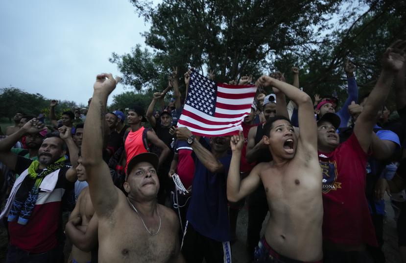 Migrantes venezolanos ondean una bandera estadounidense hacia un helicóptero de televisión que sobrevuela la zona junto al río Bravo (Grande) en Matamoros, México, el viernes 12 de mayo de 2023, un día después de que se retiraron las restricciones al asilo implementadas en la pandemia de coronavirus, conocidas como Título 42.