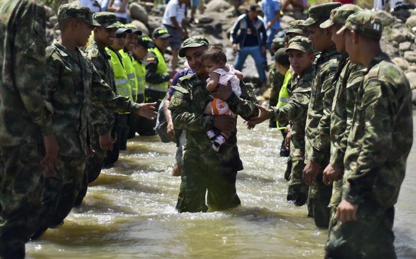 Un bebé es cargado por un militar al cruzar la frontera en el río Táchira. Cientos de colombianos están siendo deportados de Venezuela. (AFP)