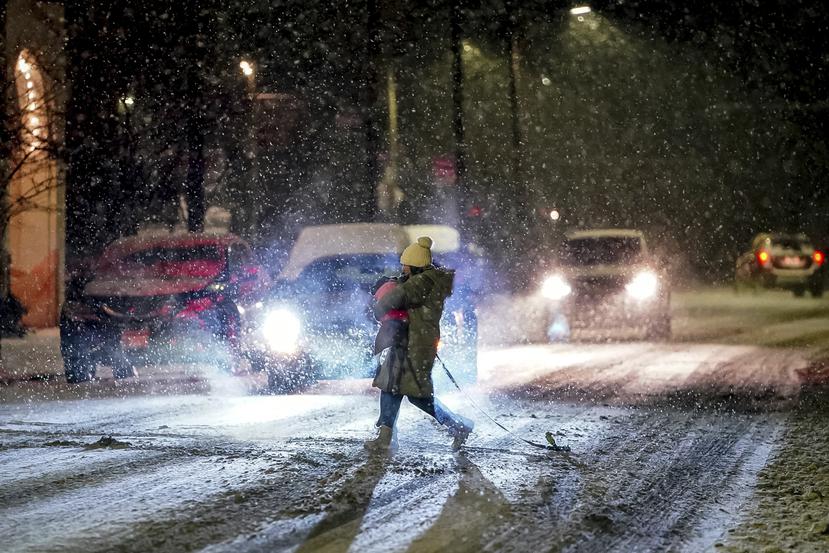 Una persona carga su perro mientras cruza la calle Butler en Pittsburgh, mientras cae nieve durante una tormenta invernal que impacta la región este de Estados Unidos.