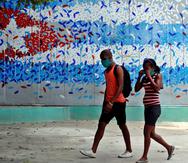 Una pareja con tapabocas camina junto a un graffitis con la imagen de la bandera cubana, en La Habana (Cuba).