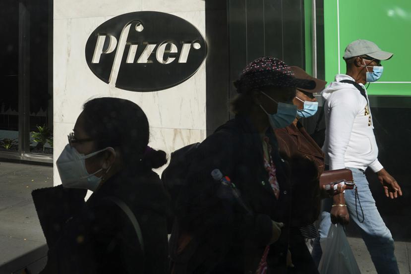 Varias personas pasan frente a un logo de Pfizer.
