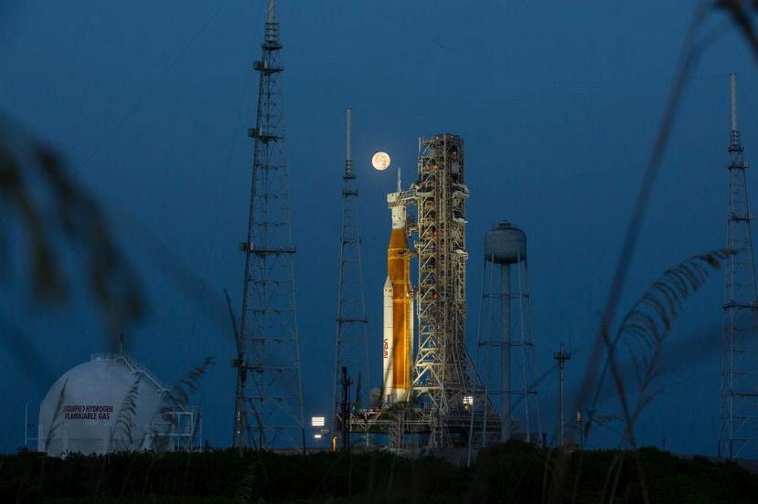 Fotografía del 14 de junio de 2022, cedida por la NASA, donde se aprecia la luna llena detrás del cohete del Sistema de lanzamiento espacial (SLS) Artemis I que lleva en lo alto la nave espacial Orion, en el Complejo de Lanzamiento 39B del Centro Espacial Kennedy.
