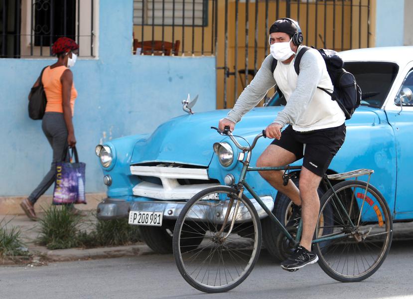 Un hombre en bicicleta y una mujer transitan por la calle usando mascarilla como medida de protección contra el coronavirus este viernes en La Habana, Cuba. (EFE)