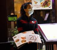 A waitress wears a protective mask as she stands at the door of a restaurant in Soho, in London, Tuesday, Sept. 22, 2020. Britain's Prime Minister, Boris Johnson, has announced that pubs and restaurants closing at 10pm, due to the spike of cases of coronavirus across the United Kingdom. (AP Photo/Alberto Pezzali)