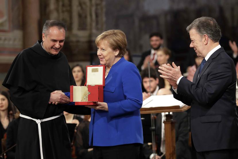 La canciller alemana Angela Merkel, centro, flanqueada por el presidente colombiano Juan Manuel Santos, derecha, y el padre Mauro Gambetti recibe el premio de la paz Lámpara de San Francisco en la Basílica de Asís, Italia.