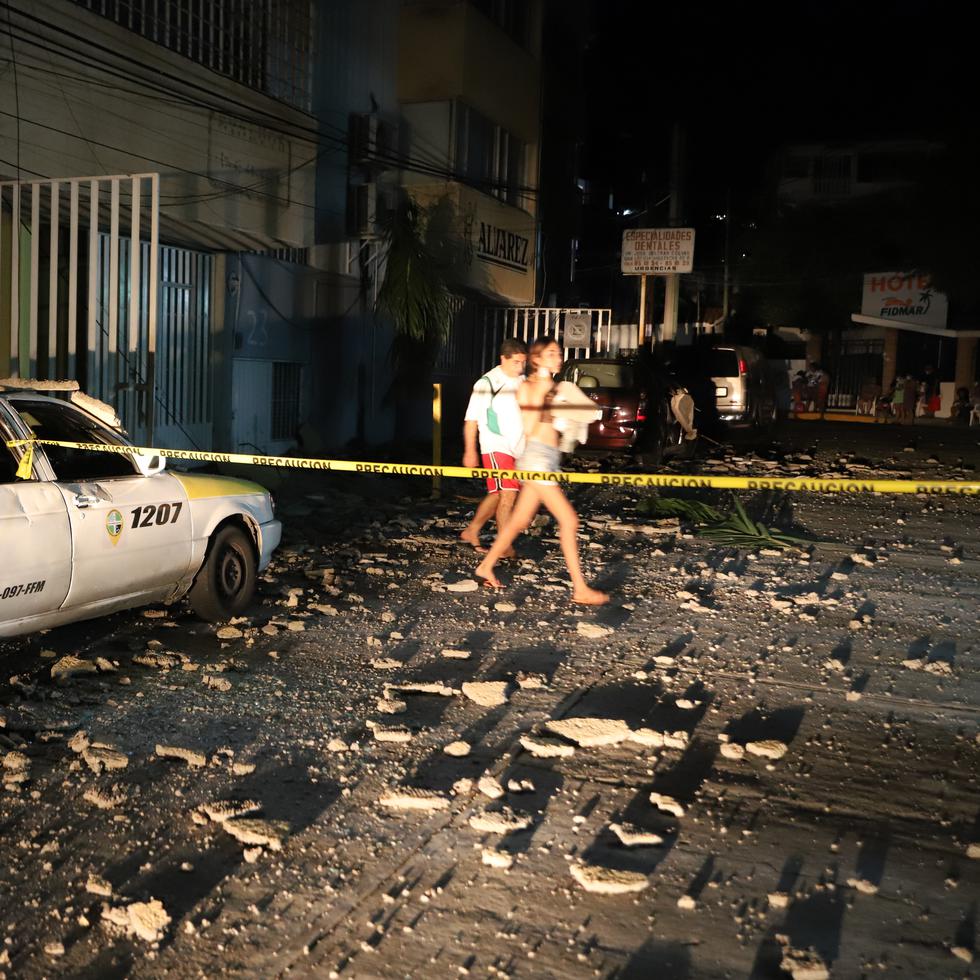 Una pareja pasa junto a un taxi que resultó dañado por la caída de escombros después de un fuerte terremoto en Acapulco, México, el martes 7 de septiembre de 2021.